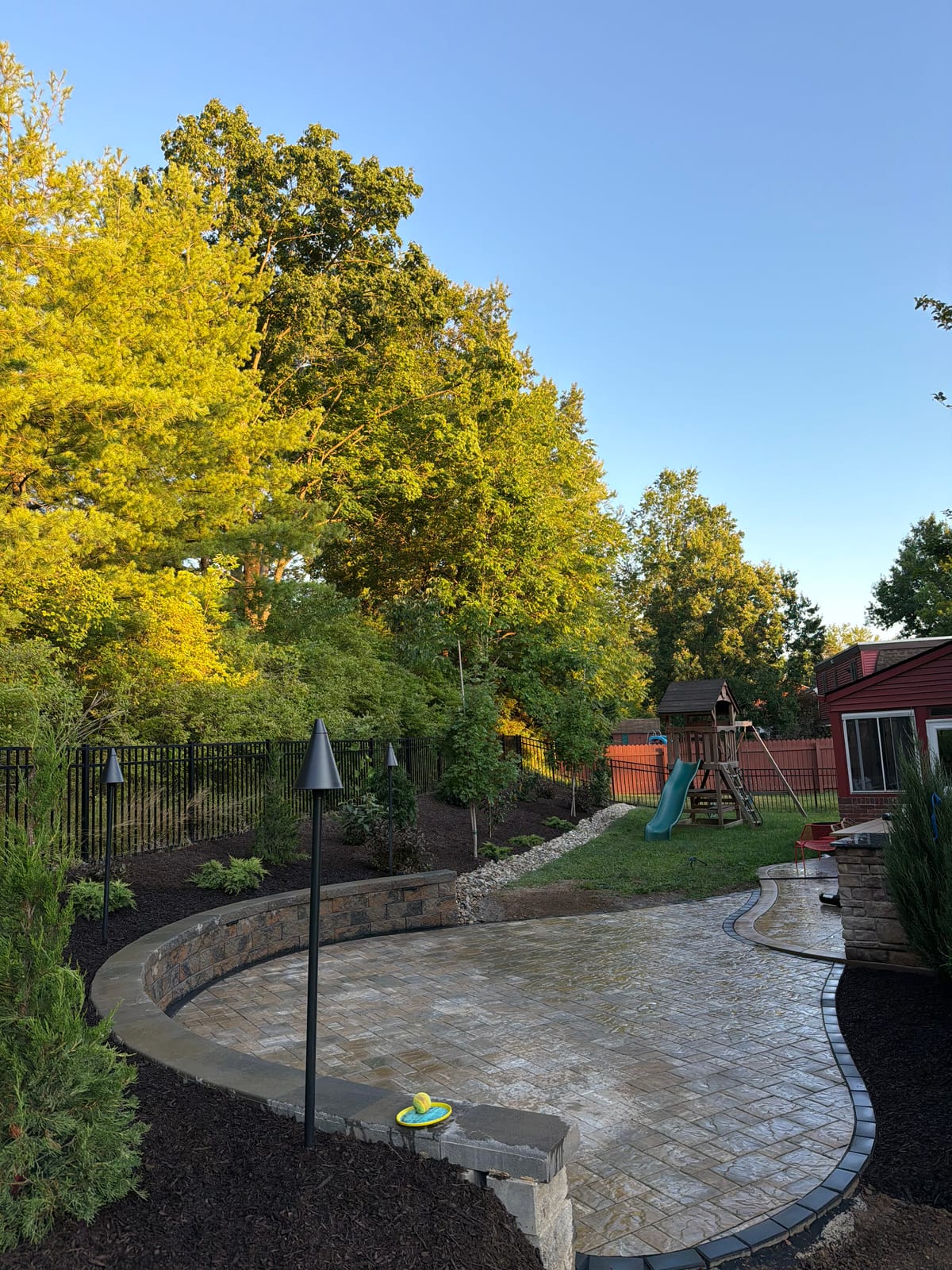 Completed curved paver patio with seat wall and landscape lighting at golden hour in McDonald, PA